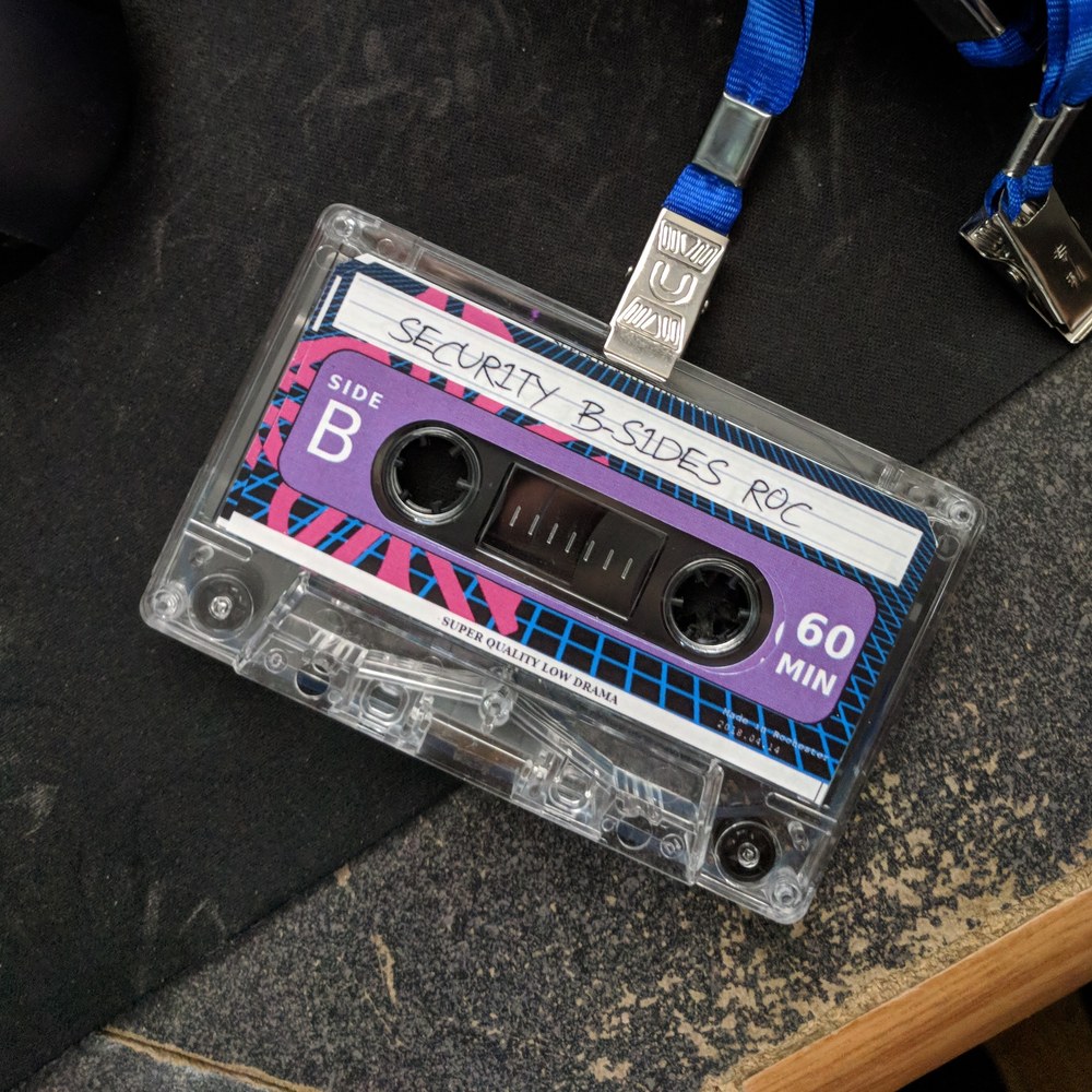 A BSidesROC cassette tape badge on a lanyard